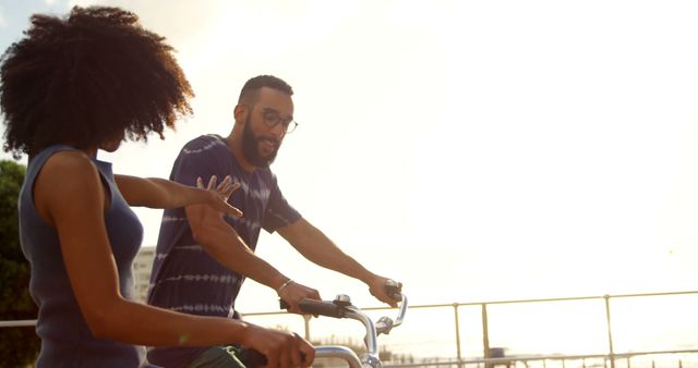 Photo showcases an African American couple having fun while biking at sunset, giving a sense of outdoor adventure and companionship. Useful for promotional material related to health, fitness, romantic getaways, and active lifestyles. Perfect for blogs, commercials, and social media posts focused on love, friendship, and healthy living.
