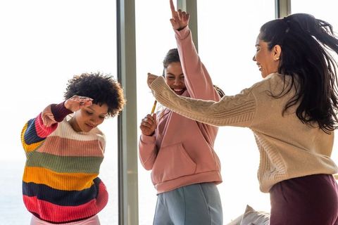 Friends dancing and laughing by seaside window wearing colorful knit sweaters and hoodie