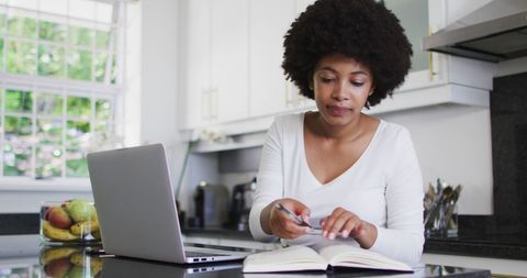 Woman Working from Home Taking Notes in Kitchen Setting