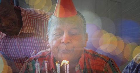 Senior Man Wearing Party Hat Blowing Birthday Candles