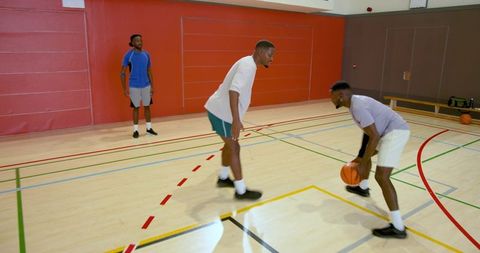 Competitive one-on-one basketball drill on indoor hardwood court with defender