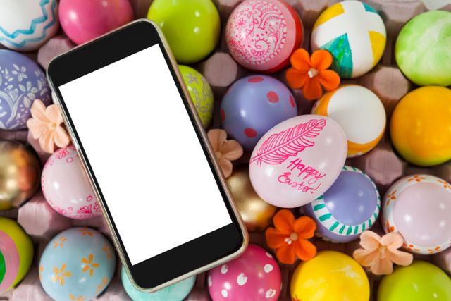 Mobile phone with blank screen surrounded by vibrant, painted Easter eggs and small flowers. Ideal for Easter promotions, holiday greetings, digital communication themes, and festive marketing materials.