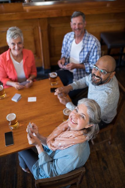 Group of friends enjoying a casual game of cards while having beer in a bar. Perfect for depicting social gatherings, leisure activities, and senior lifestyle. Ideal for use in advertisements, blogs, and articles about friendship, relaxation, and social events.