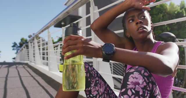 Tired african american woman with water bottle taking a break from running on the city bridge. fitness sports and active lifestyle concept