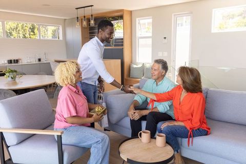 Diverse friends delivering gifts and shaking hands in modern bright open-plan living room