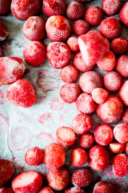 Frozen strawberries displayed closely on a white surface with some partially covered in ice crystals, highlighting their texture. Ideal for food blogs, advertisements for frozen berry products, or recipes requiring frozen fruit.