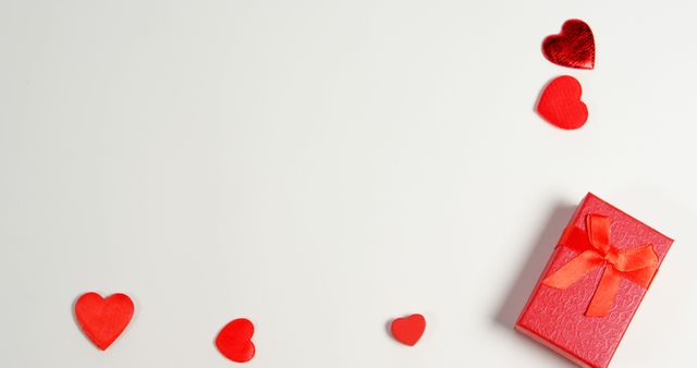 Red hearts and a gift box with a bow are arranged on a plain background, with copy space. This setup is often associated with romantic celebrations such as Valentine's Day or anniversaries.