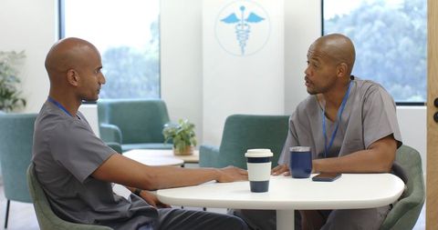 Two african american healthcare workers talking and relaxing in clinic breakroom