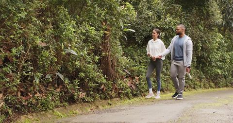 Couple walking hand in hand on mossy paved trail through lush green woodland pathway
