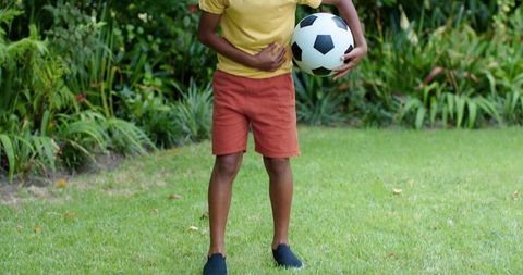 African american boy standing on lawn holding soccer ball backyard playtime and fitness