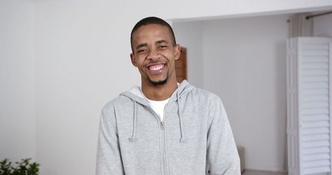 Smiling Man in Gray Hoodie Expressing Warmth at Home