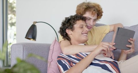 Joyful couple at home using digital tablet on sofa