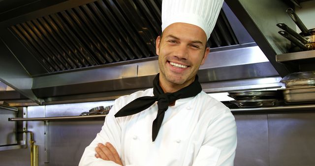 Professional chef standing with arms crossed in commercial kitchen, smiling confidently. Suitable for use in culinary school promotions, restaurant adverts, food blogs, or articles related to gastronomy and chef career success.