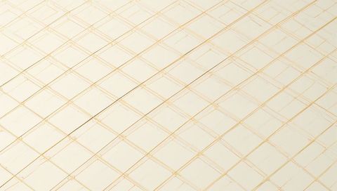 Creamy ivory tiles forming diagonal gold grid with subtle grout scuffs and glossy finish