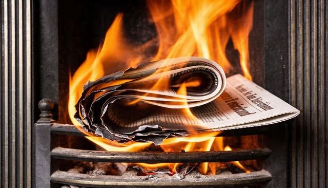 Burning folded newspaper curling on fireplace grate with bright flames and charred edges