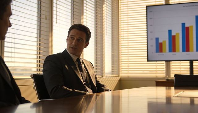 Executive speaking in sunlit boardroom during presentation with colorful bar chart