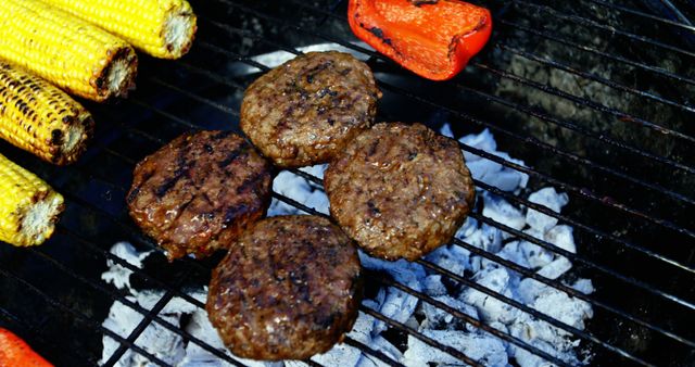 Impress at your next BBQ with images of beef burgers grilling over charcoal alongside corn and bell peppers. Ideal for cookout promotions, outdoor cooking articles, and summer recipe features.