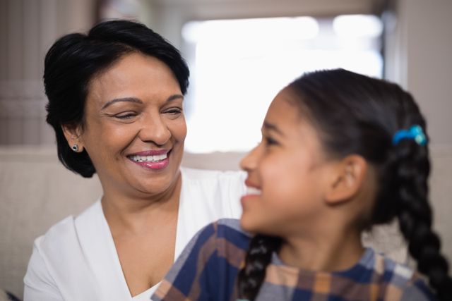 This image captures a joyful moment between a grandmother and her granddaughter at home. Ideal for use in family-oriented content, advertisements promoting family values, or articles about intergenerational relationships and bonding. The warm and affectionate interaction can also be used in healthcare or wellness contexts to highlight the importance of family support.