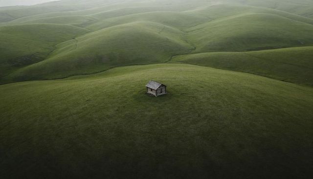 Solitary wooden cabin perched on rolling green hills in misty moorland