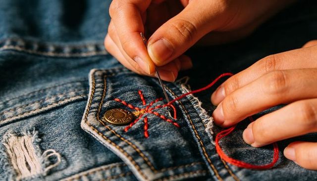 Hand stitching red star on denim pocket for upcycled fashion repair