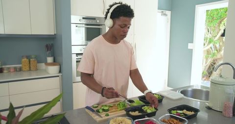 Young african american man preparing healthy meal prep bowls in bright modern kitchen