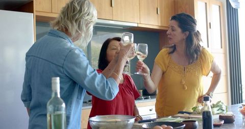Women toasting white wine while preparing meal together at bright kitchen countertop