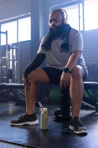 African american man resting on bench after kettlebell workout wearing headphones
