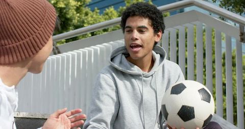 Young men talking on outdoor steps holding soccer ball casual friendship and teamwork
