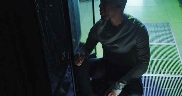 African American male technician working with a laptop in a business server room, focusing on digital information storage and communication network technology. This is ideal for showcasing IT professional work environments, server maintenance procedures, or data management. It can also be used in materials highlighting careers in technology, network security, or data center operations.