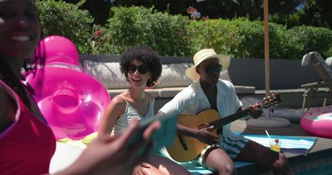African american friends enjoying poolside party playing guitar and taking smartphone selfie