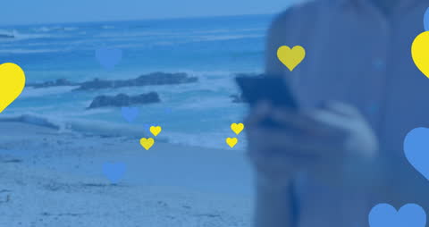 Colorful Heart Icons by Ocean with Person Using Phone
