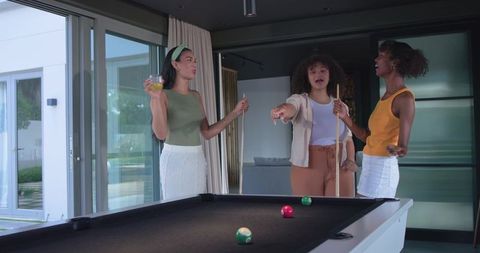 African american women playing pool and laughing in modern home lounge