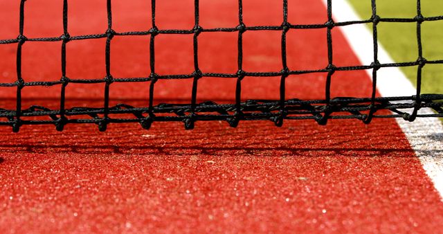 This detailed view of a tennis net on a red clay court is ideal for sports-related content, tennis tutorials, training materials, or fitness inspiration articles. It captures an authentic element of the tennis environment and highlights the fine details of the tennis net against the vibrant red surface.
