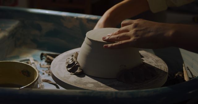 Side view mid section of a young Caucasian female potter turning a clay dish on a potters wheel and shaping it with a tool in a pottery studio
