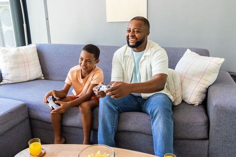 African american father and son playing video games on couch enjoying family time