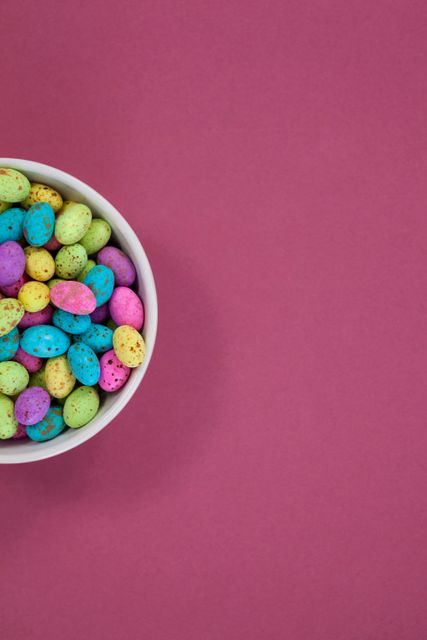 Colorful chocolate Easter eggs in a bowl on pink background