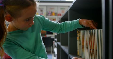 Young girl searching for favorite book on library shelf