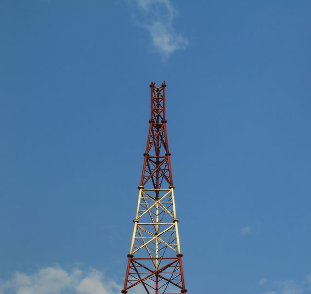 Communications tower standing prominently against a clear blue sky, perfect for illustrations of telecommunications infrastructure, communication technology, and broadcasting. Suitable for educational materials, industry presentations, and articles related to communications technology and wireless transmission.