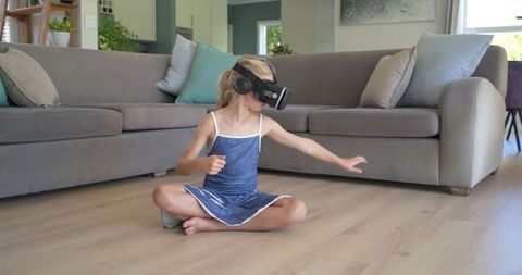 Young girl experiencing virtual reality while sitting on living room floor reaching out