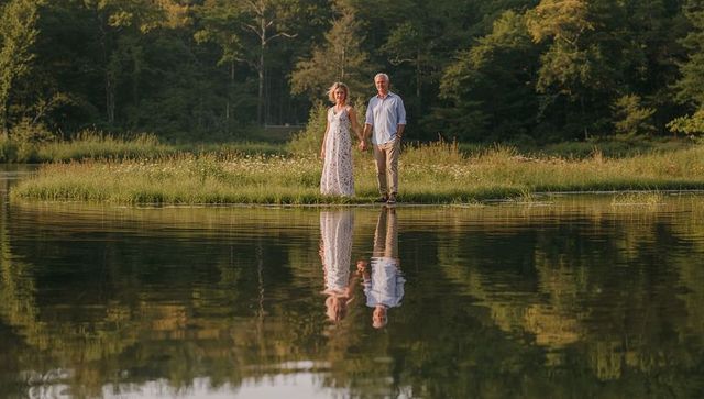 Mature Couple Holding Hands on Lakeshore at Golden Hour with Mirror Reflection