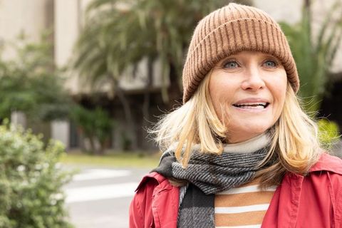 Smiling middle-aged woman wearing beanie and red jacket standing on urban walkway