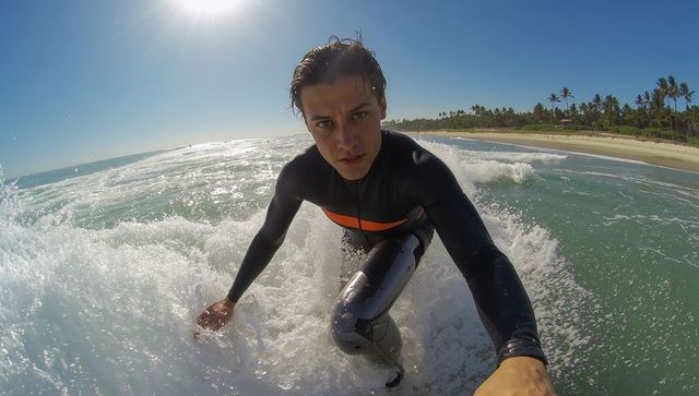 Surfer riding wave pov close-up, black wetsuit with orange stripe, tropical beach