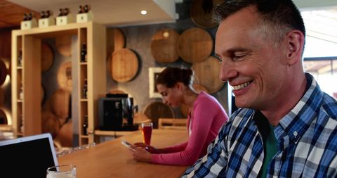 Smiling Man Working on Laptop in Rustic Bar with Wine Barrels - Download Free Stock Images Pikwizard.com