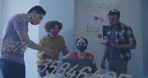 Diverse team collaborating at laptop wearing colorful masks during office meeting