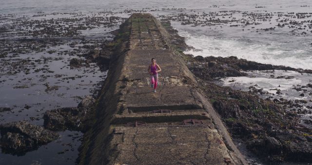 Woman Jogging on Seaside Promenade Amidst Rocky Shoreline - Download Free Stock Images Pikwizard.com