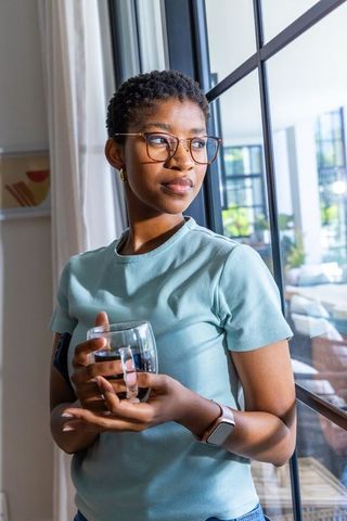 African american woman standing by window holding glass mug in sunlit minimalist room