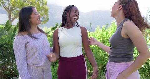 Laughing friends wearing athleisure in sunny park by foothills, multicultural trio