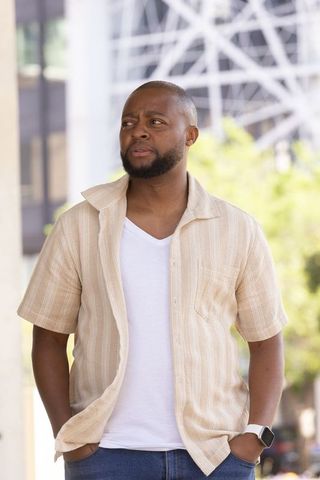 African american man standing in urban plaza wearing beige shirt checking smartwatch
