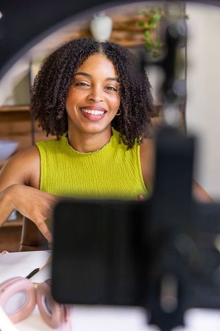 Smiling black content creator presenting on smartphone in home studio lime green top