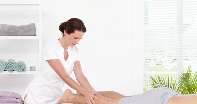 Massage therapist is working on a client's leg in a serene wellness center. Ideal for content related to physical therapy, spa treatments, wellness services, relaxation techniques, and therapeutic massage sessions.